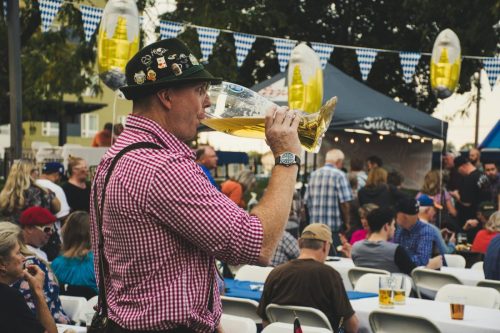 Man enjoying a large beer mug at an Oktoberfest celebration outdoors with a lively crowd.